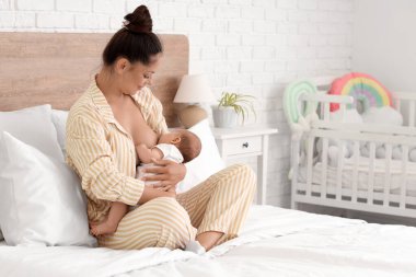 Güzel, genç ve mutlu bir kadın bebeğini yatak odasında emziriyor.