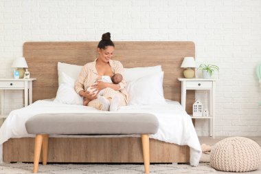 Güzel, genç ve mutlu bir kadın bebeğini yatak odasında emziriyor.