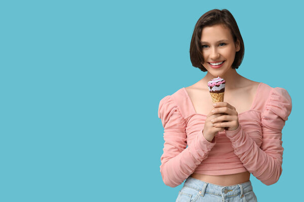 Beautiful young woman with sweet ice-cream in waffle cone on blue background