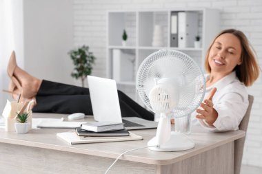 Bilgisayarı, bir bardak suyu ve elektrikli vantilatörü olan güzel, olgun bir iş kadını.