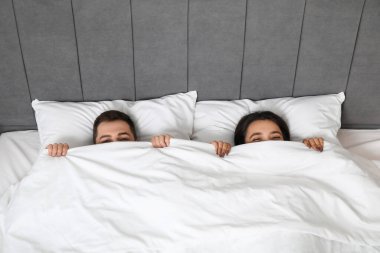 Yatak odasında battaniyenin altında uzanan, sevgi dolu genç bir çift.