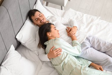 Kocasıyla birlikte yatakta uyuyan genç bir kadın.