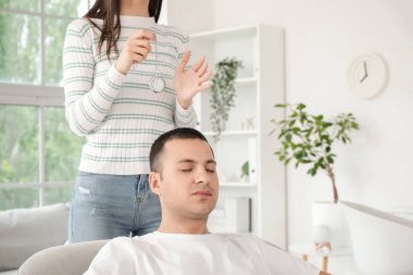 Cep saati olan bir kadın psikolog ofisteki koltukta genç bir adamı hipnotize ediyor.