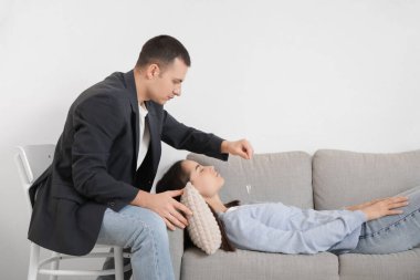 Ofisteki kanepede genç bir kadını hipnotize eden sarkacı olan erkek psikolog.