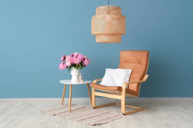 Sehpanın üzerinde pembe şakayık çiçekleri olan vazo şık oturma odasındaki koltuğun yanında.