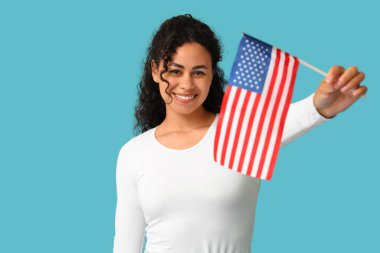 Mavi arka planda Amerikan bayrağı olan güzel, mutlu, Afro-Amerikan bir kadın.