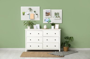 Beyaz çekmeceleri, çiçekleri, fotoğraf çerçeveleri ve tahtaları olan şık bir oturma odası.