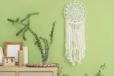 İçinde okaliptüs dalları olan vazo, yeşil duvarın yakınındaki çekmece çekmecesinde, yakın plan.