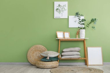 Okaliptüs dalları ve yeşil duvarın yanındaki bankta duran fotoğraf çerçeveli vazo.