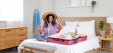 Genç Afro-Amerikalı bir kadın otel odasında bavulunu giysileriyle açıyor.