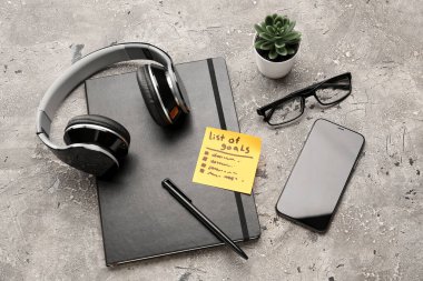 Hedef listesi, not defteri, kulaklık, cep telefonu ve gözlük içeren yapışkan not grunge arkaplanda