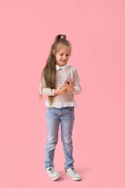 Pembe arka planda cep telefonu kullanan süveter giyen şirin küçük kız.