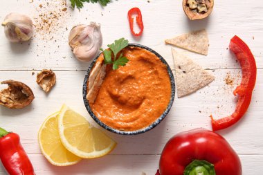 Bir kase lezzetli muhammara ve beyaz ahşap arka planda malzemeler.