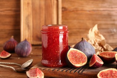 Kavanoz dolusu tatlı incir reçeli ve ahşap arka planda taze meyveler.