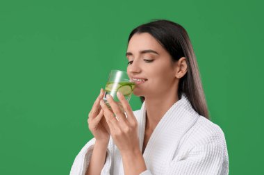 Yeşil arka planda bir bardak salatalık suyu olan genç bir kadın, yakın plan.