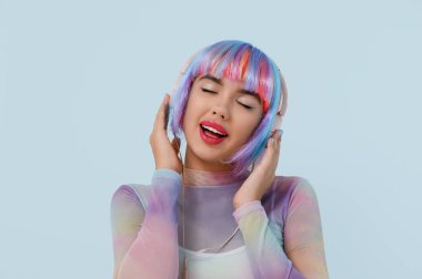Renkli peruklu güzel bir kadının portresi mavi arka planda müzik dinliyor.