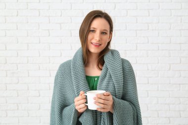 Beyaz tuğlalı arka planda bir fincan çay ve ekoseli genç kadın.