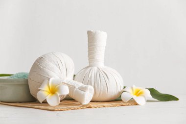 Beyaz duvarın yanındaki masada bitki torbaları ve çiçeklerle güzel bir spa kompozisyonu.