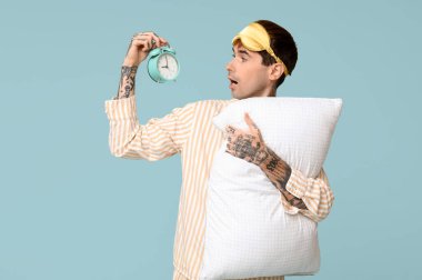 Mavi arka planda yastıklı ve çalar saati olan pijamalı dövmeli genç bir adam.