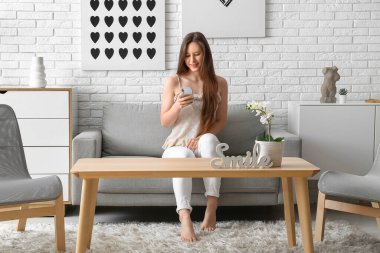 Evdeki koltukta cep telefonu kullanan genç bir kadın.