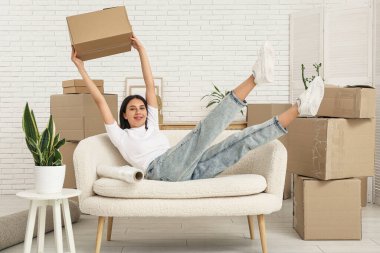Yeni dairede kanepeye uzanmış karton kutulu neşeli genç bir kadın. Taşınma konsepti