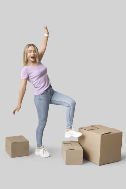 Gri arka planda karton kutuları olan mutlu genç bir kadın. Yeni ev konseptine geçiyoruz.