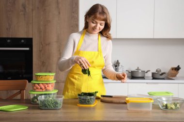 Kadın mutfakta donmak için plastik kabın içine ıspanak koyuyor.