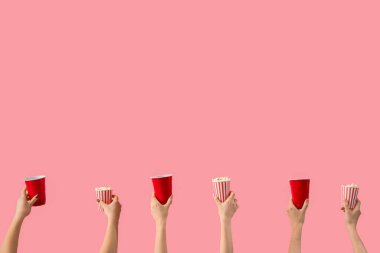 Patlamış mısırlı kovaları tutan eller ve pembe arka planda içkiler