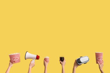 Patlamış mısır, kola, VR kulaklık ve sarı arka planda megafon bulunan kovaları tutan eller.