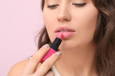 Güzel genç bir kadın pembe ruj sürerken arka planda, yakın plan