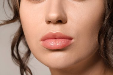 Beautiful young woman with nude lipstick on grey background, closeup clipart