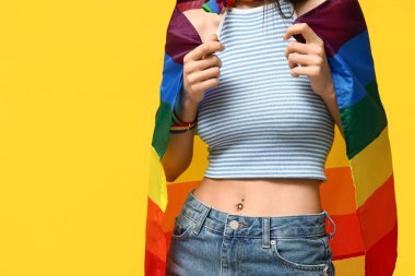 Sarı arka planda piercing göbeği ve LGBT bayrağı olan güzel bir genç kadın, yakın plan.