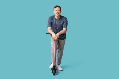 Mavi arka planda modern elektrikli scooter kullanan genç bir adam.