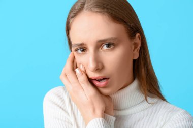 Mavi arka planda diş ağrısından muzdarip güzel genç bir kadın, yakın plan.