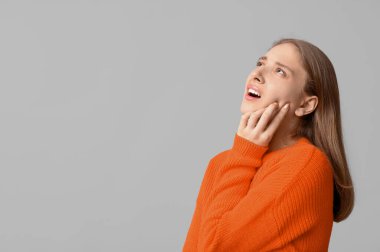 Gri arka planda diş ağrısı çeken genç bir kadın.