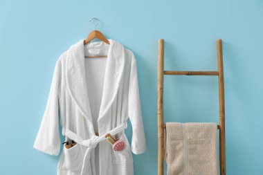 Mavi arka planda farklı banyo malzemeleri asılı beyaz bornoz.