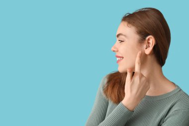 Mutlu genç kadın mavi arka planda işitme cihazına işaret ediyor.