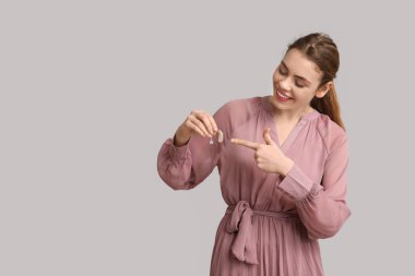 Gri arka planda işitme cihazına işaret eden güzel genç bir kadın.