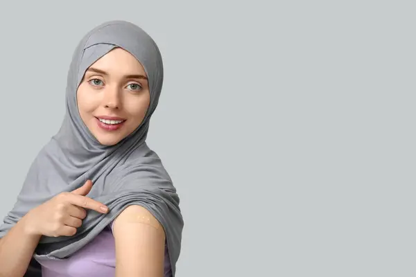 stock image Muslim woman with medical patch on arm against grey background. Vaccination concept