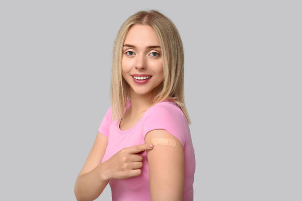 Young woman with medical patch on arm against grey background. Vaccination concept