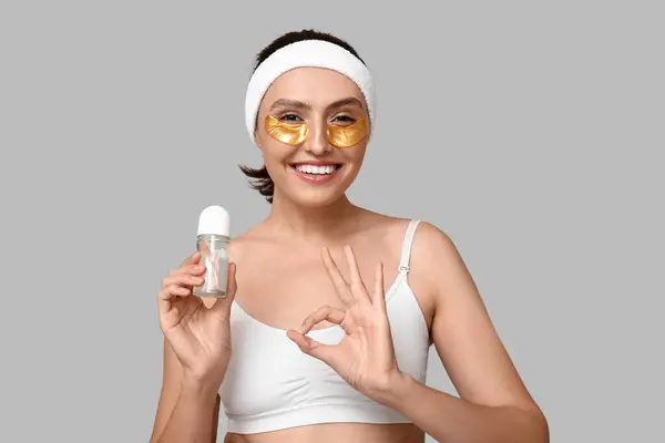 stock image Young woman with roll-on deodorant showing OK on light background