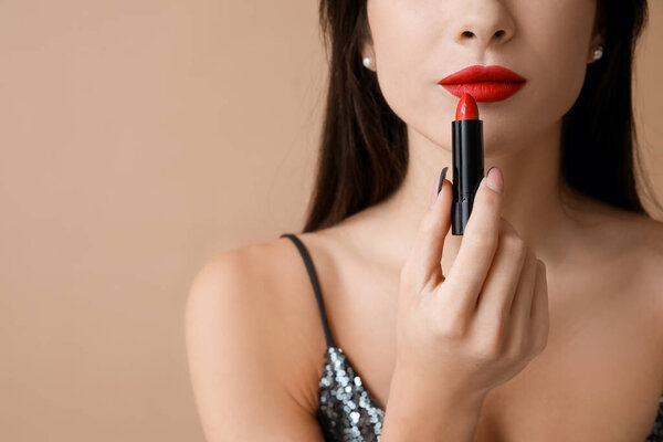Красивая молодая женщина наносит красную помаду на коричневый фон, крупным планом