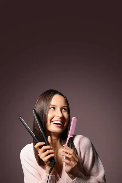 stock image Beautiful young woman with hair straightener and comb on pink background