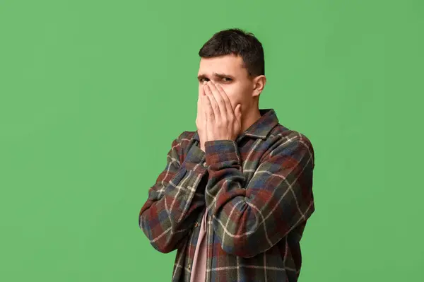 stock image Handsome young man feeling bad smell on green background