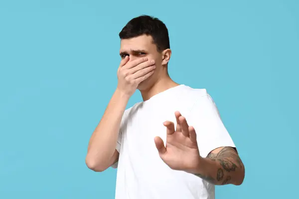 Stock image Handsome young man feeling bad smell on blue background