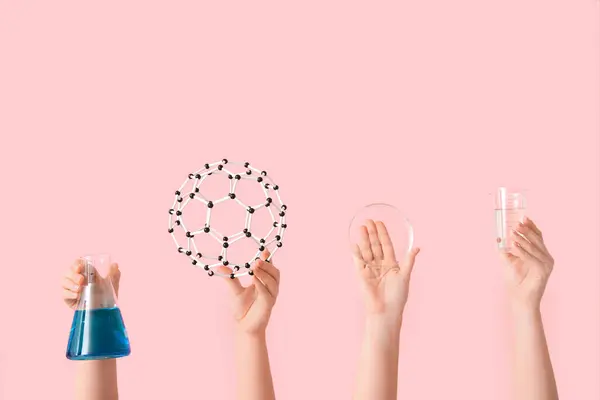 stock image Female hands holding filled flask with molecular model, Petri dish and measuring cup on pink background. Chemistry lesson concept