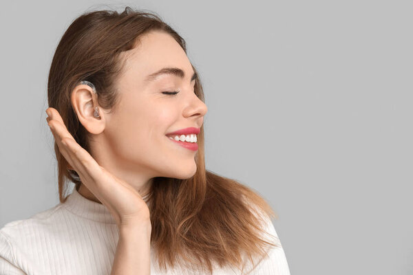 Счастливая молодая женщина со слуховым аппаратом на сером фоне