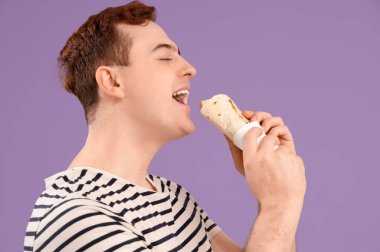 Genç adam mor arka planda donör kebabı yiyor.