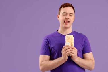 Genç düşünceli bir adam mor arka planda donör kebabı tutuyor.