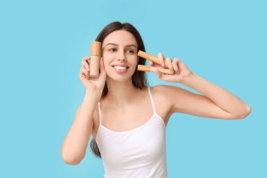 Beautiful young woman holding set of decorative cosmetics on blue background